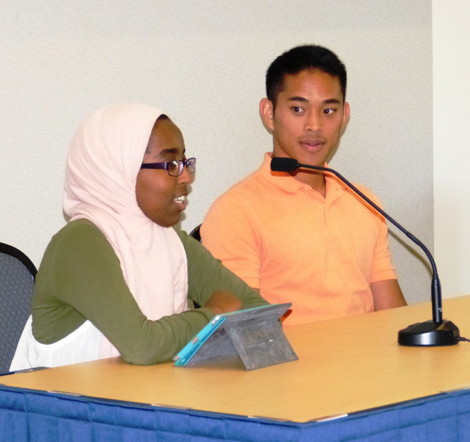 Male and female student sitting at a table. The young woman is speaking