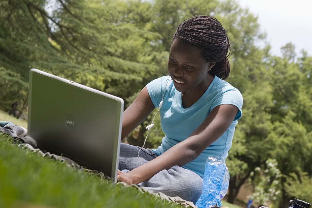 Female student studying in the arboretum with laptop and microphone