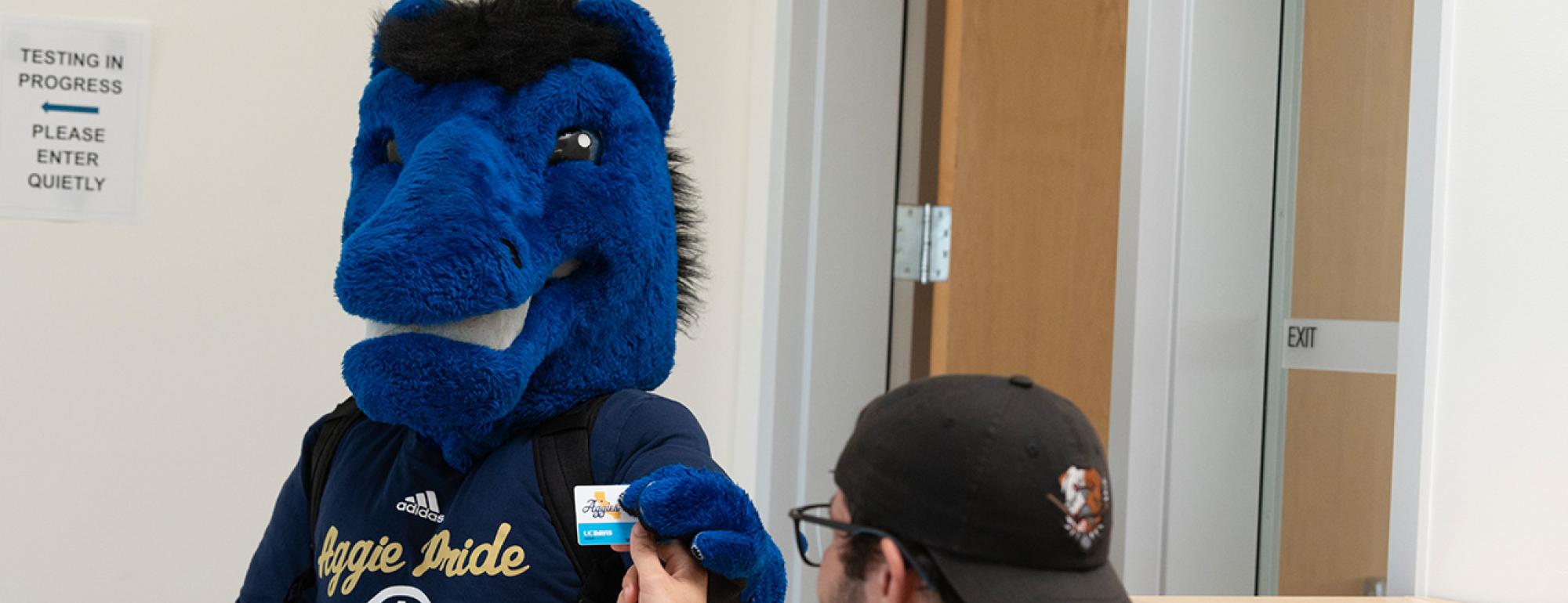 Man in cap photographing a Gunrock mascot head behind a reception counter