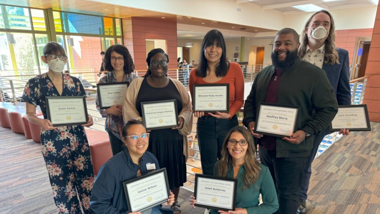 A group of 8 academic advisors stand in two rows holding up award certificates.