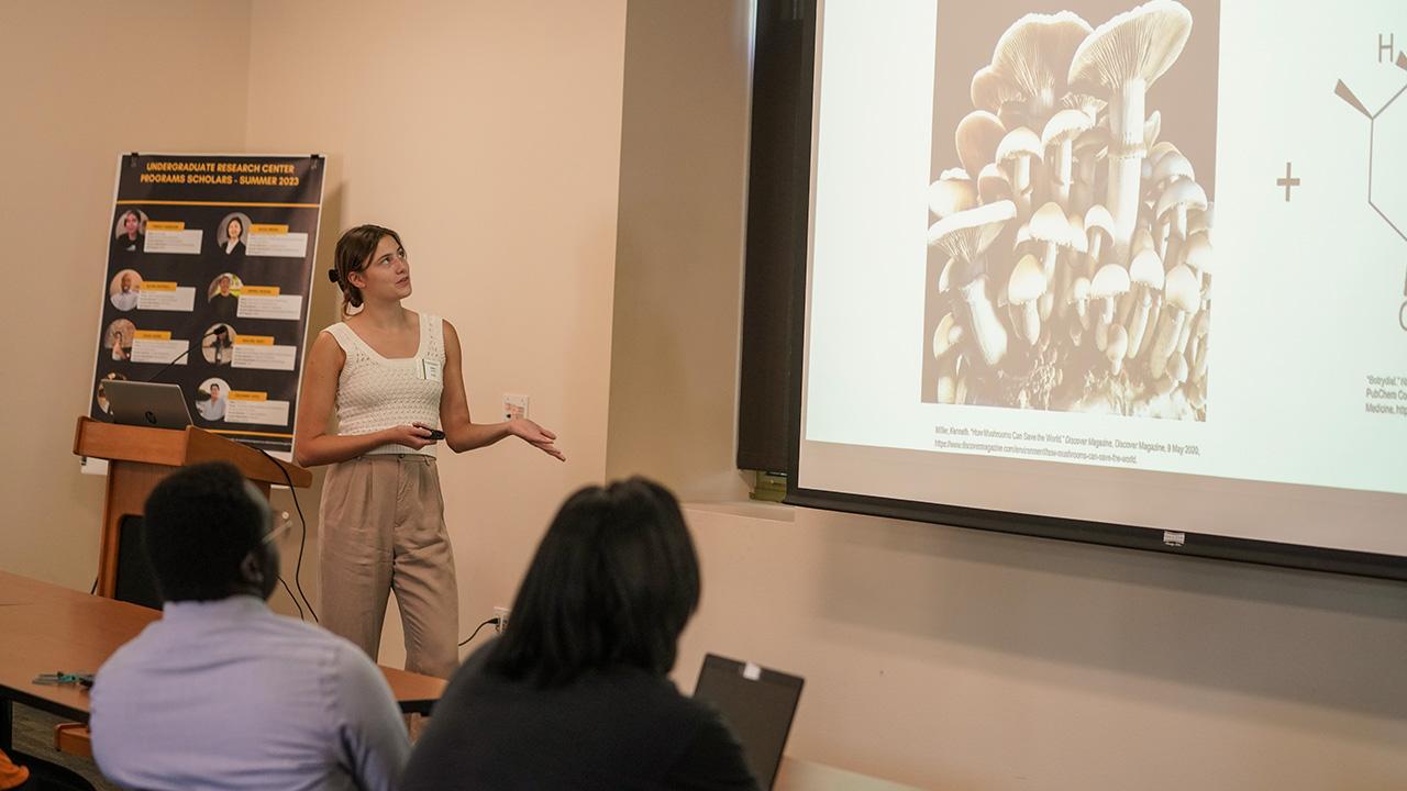 Undergraduate student Julia Cook points to her powerpoint explaining her Plant Sciences research at the 2023 Summer Undergraduate Resarch Program