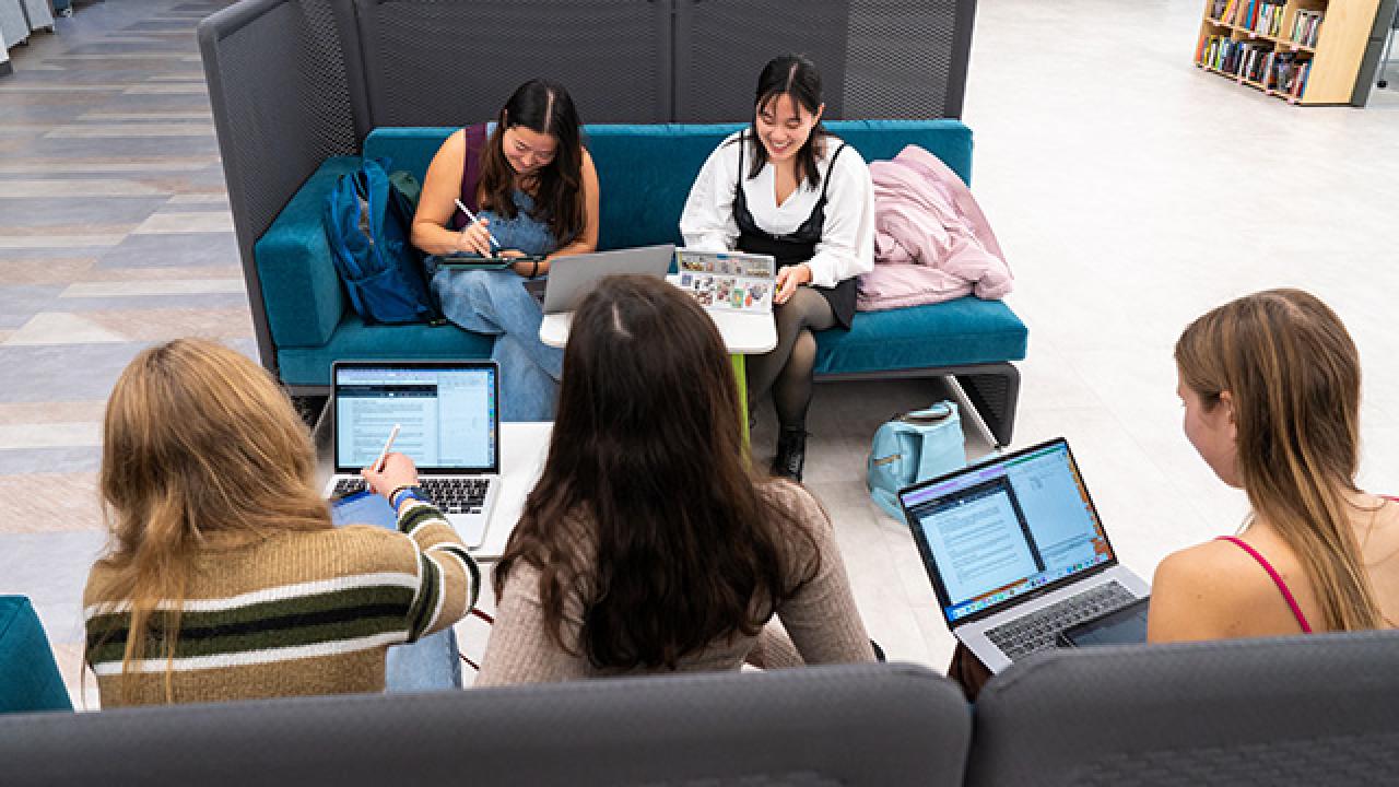 Looking down on a group of students seated around a table who are all working on laptops.