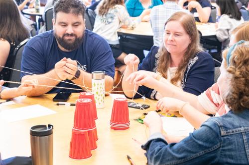 A diverse team of advisors work to build a structure with red plastic cups at their round table.
