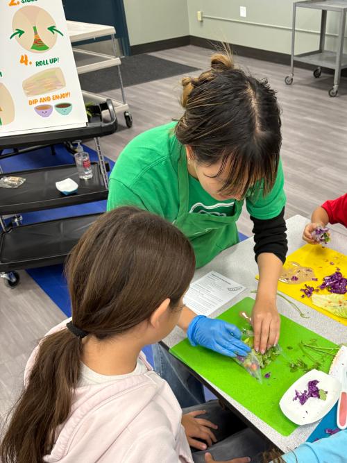 Adult in green shirt guiding child with clay craft at a classroom table