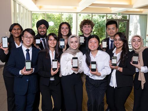 A team of 11 undergraduate students hold their smart phones, showing the app they invented.