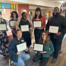 A group of 8 academic advisors stand in two rows holding up award certificates.